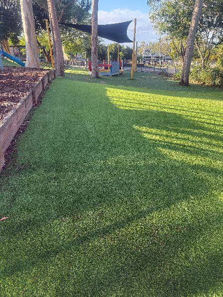 Artificial grass after being swept with 602 Garland Lawn sweeper with playground equipment in the background
